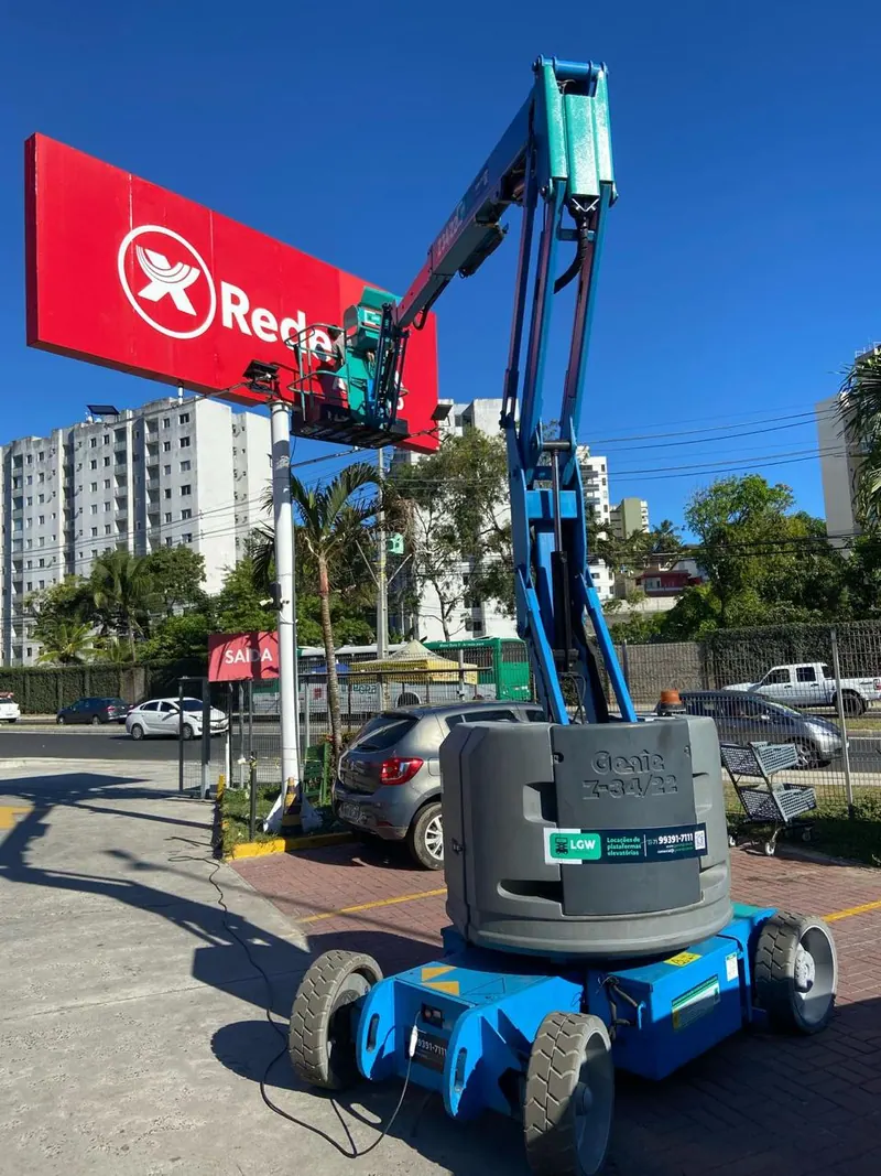Plataforma articulada azul erguida junto a um letreiro vermelho de supermercado