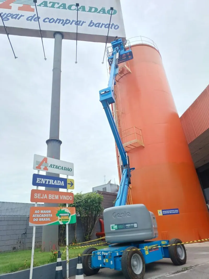 Plataforma articulada azul levantada ao lado de um letreiro alto de atacado
