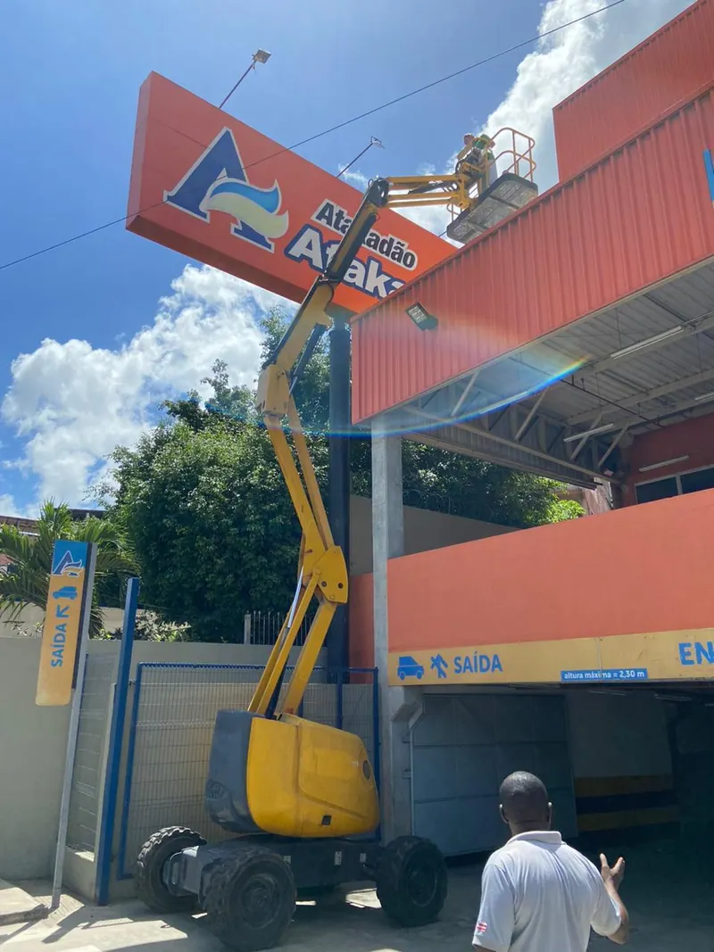 Plataforma articulada amarela erguida junto ao letreiro laranja de um atacado