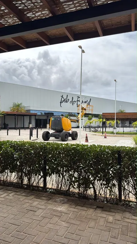 Plataforma articulada amarela ao fundo, na entrada de um shopping, sob um pergolado
