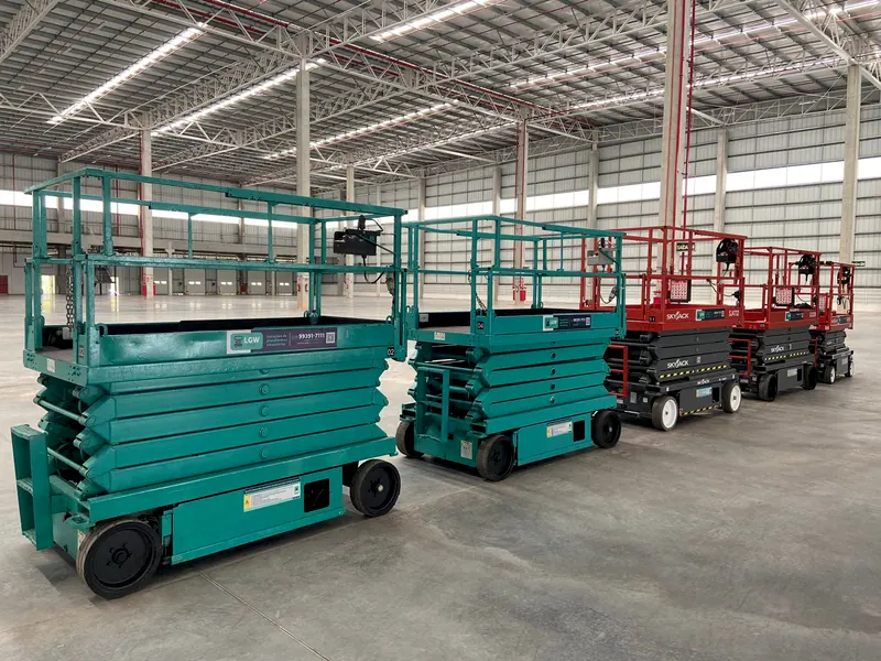 Plataformas tesoura verdes e vermelhas enfileiradas num galpão grande